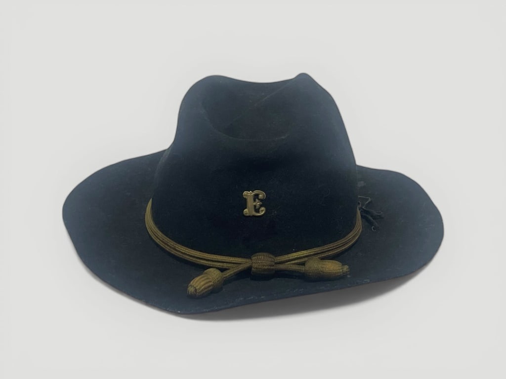 Early Black Felt Hat with Gold Cord: Black felt hat featuring a gold cord accent tied at the front with decorative knots and a prominent 'E' emblem on the front. Inner band lined in brown material. Measures approximately 14.5 W x 5 H.