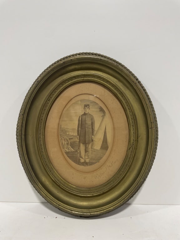 Antique Civil War Soldier with Inscription 1863: An oval-shaped framed photograph featuring a soldier in uniform with a rifle. The image appears to be an older print and includes an inscription reading "1863" and "Moses Hallas" on the matting.