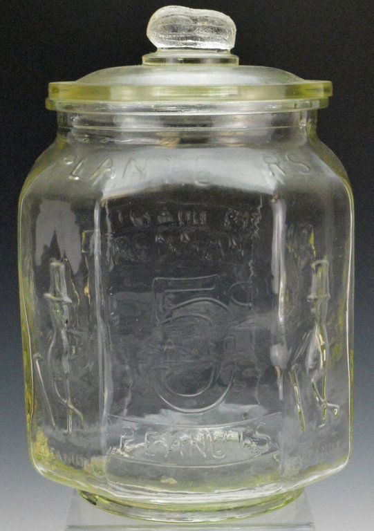 Early Large Glass Planters 5c Peanut Jar: Early 20th century large glass country store Planters peanut jar. Retains original lid with peanut finial. Has 2 small chips to underside of the rim of the lid. Has a great looking air bubble on one s