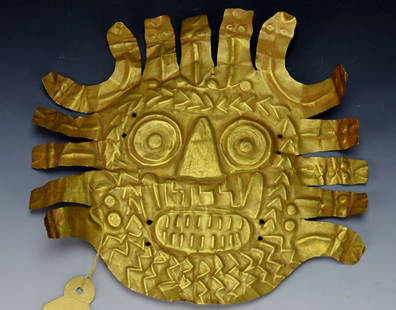 Nazca Gold Ornament : Sotheby's: c. 300-600, the thin hammered sheet probably used as a headdress ornament, in the form of a ferocious feline deity's head, densely marked in repousse with whiskered open mouth baring teeth, the ruff i