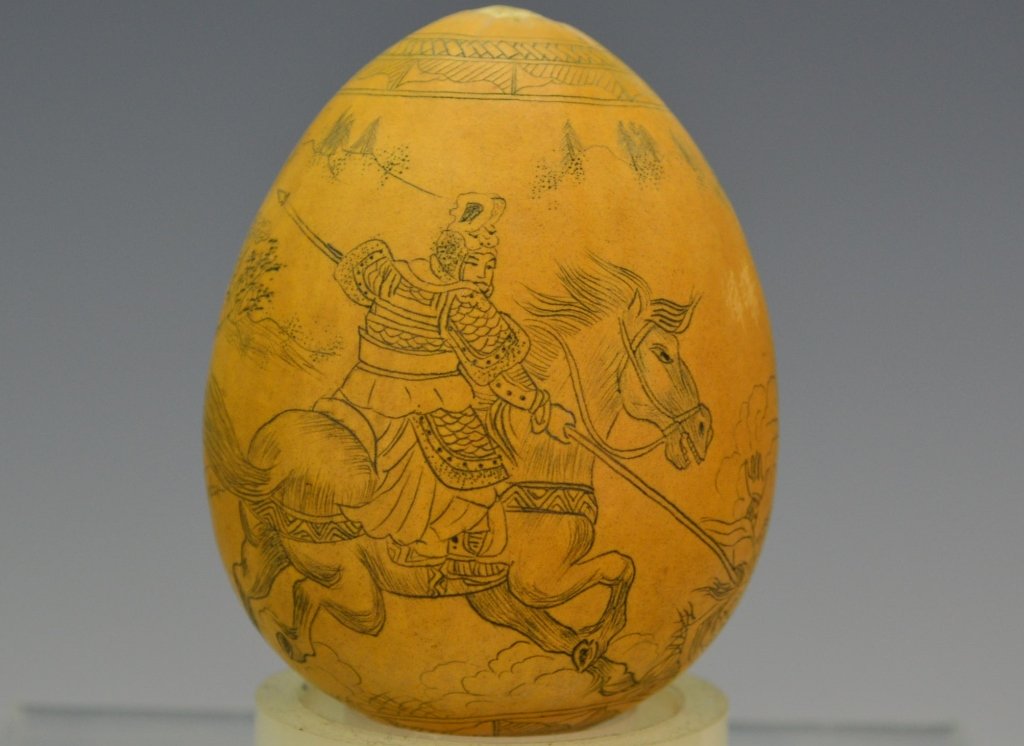 Etched Japanese Nut: Ovoid form finely decorated with borders to top and bottom detailed landscape with sprawling hills and a samurai on horseback lancing a fallen opponent. Measures 2.75" T