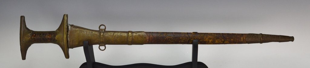 Jiboula Sword: Morocco circa 19th century. The blade has a triple blood groove as well as six "x" and small dot markings. The blade and sheath are in good condition. It is leather with design inlaid copper mounts. T