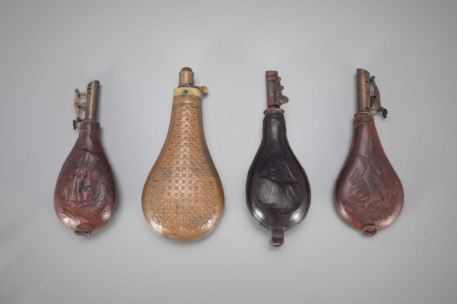 Four Powder Flasks: Four Powder Flasks largest is 8 1/2 in. tall The largest powder flask is metal and bears a Dixon insignia. The leather flasks each display a different embossed scene: a dog, a rabbit, and a dog holdin