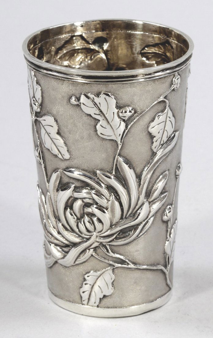 Becher: Becher China/wohl Shanghai, um 1890. 900er Silber. Punzen: Herst.-Marke. H. 9,5 cm. Gew.: 90 g. Kl. Dellen. Aufwendig verzierter Korpus mit Blumendekor und Wappenschild auf gerautem Grund.