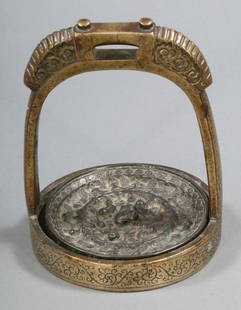 Spiegel mit Henkelschale Wohl China, Qing Dynasti: Spiegel mit Henkelschale Wohl China, Qing Dynastie. Bronze. Spiegel: H. 1 cm. D. 11,5 cm. Schale: H. 17 cm. Spiegel mit Frosch- Löwen- und Schwalbendarstellungen, dazwischen immer wieder Traubenmotiv