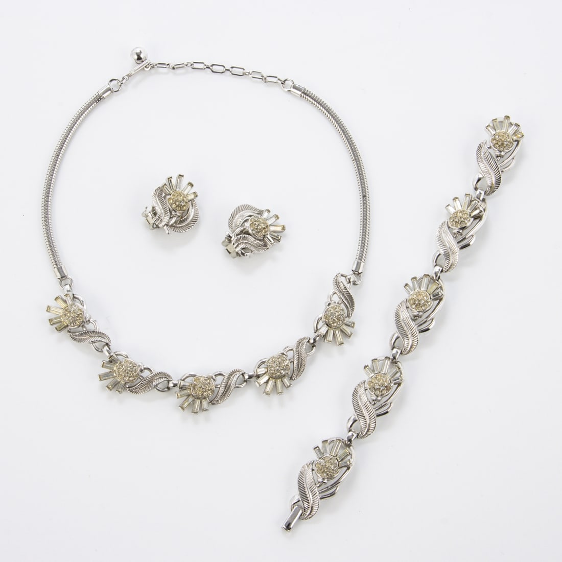 TRIFARI Alfred Philippe - Vintage Schmuckset (3 Teile): TRIFARI Alfred Philippe - Vintage Schmuckset (3 Teile)New York, um 1960 - 1970. Collier, Armband, und Paar Ohrclips. Metall, silberfarben mit Strass. Collier-L. 40 cm. B. ca. 1,5 cm. Armband-L.: 17,5
