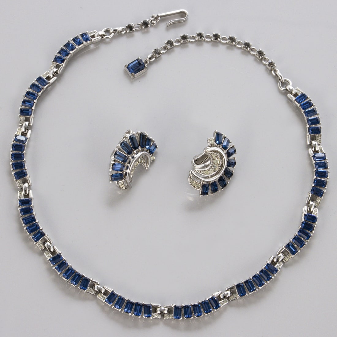 TRIFARI Alfred Philippe - Vintage Saphire-Schmuckset (2 Teile): TRIFARI Alfred Philippe - Vintage Saphire-Schmuckset (2 Teile)New York, 1960 - 1970. Collier und Paar Ohrclips. Metall, silberfarben mit Faux-Saphiren und Strass. Collier-L. 36 cm, B. ca. 7 mm. Ohrcli