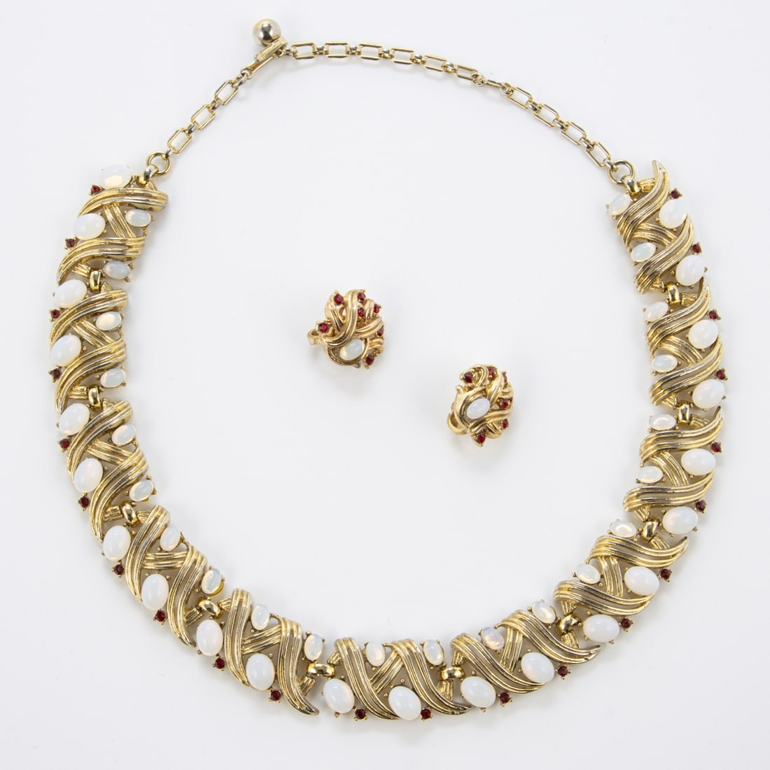 TRIFARI Alfred Philippe - Vintage Schmuckset (2 Teile): TRIFARI Alfred Philippe - Vintage Schmuckset (2 Teile)New York, um 1960. Collier und Paar Ohrclips. Metall, goldfarben mit mondsteinfarbenem Strass u. kleinem rotfarbenen Strass. Collier-L. 33 - 42 cm