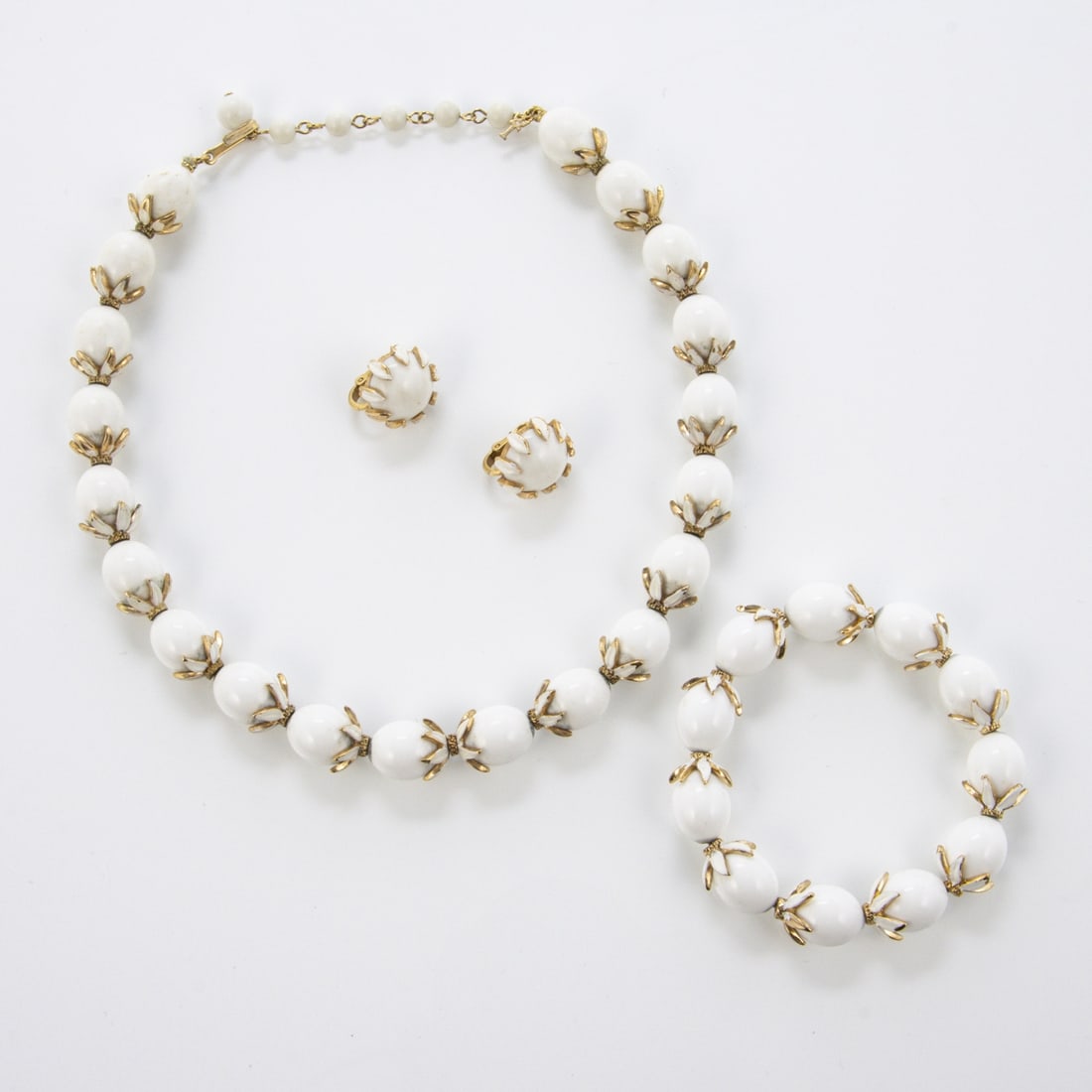 TRIFARI Alfred Philippe - Vintage Parure Schmuckset (3 Teile): TRIFARI Alfred Philippe - Vintage Parure Schmuckset (3 Teile)New York, um 1960. Collier, Armband und Paar Ohrclips. Metall, weisse Kunststoffperlen u. goldfarbene Kelchblaetter, Emaille. Collier m. J-