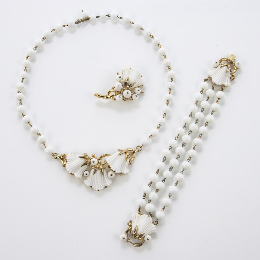 TRIFARI Alfred Philippe - ''Beau Belles'' Parure Schmuckset (3 Teile): TRIFARI Alfred Philippe - ''Beau Belles'' Parure Schmuckset (3 Teile)New York, um 1953. Collier, Armband, Brosche. Metall, goldfarben mit Milchglas. Collier-L. 43 cm, B. ca. 3 cm. Brosche-L. 4,5 cm, s