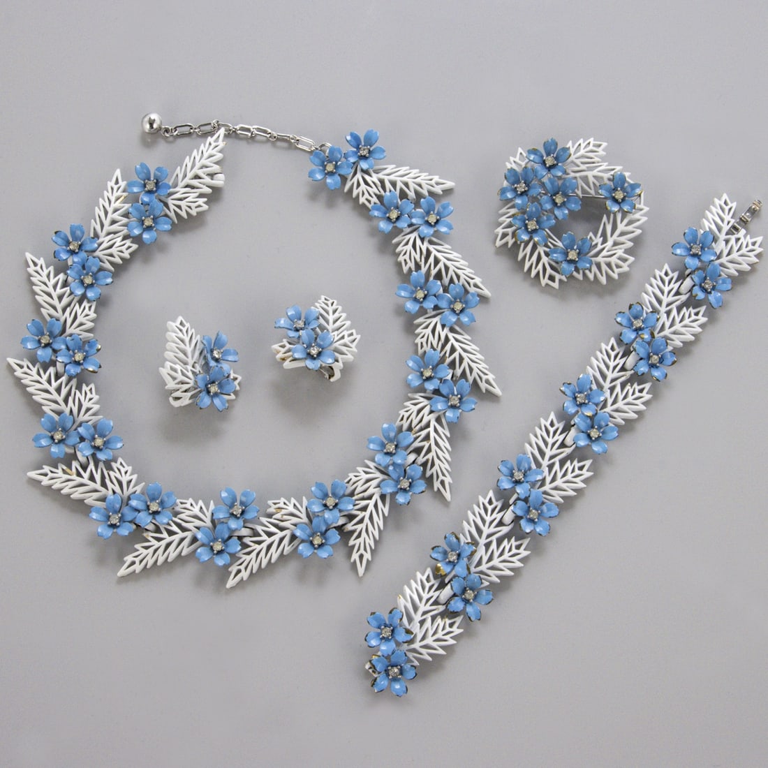 TRIFARI Alfred Philippe - Bluetenfarn Parure Set (4 Teile): TRIFARI Alfred Philippe - Bluetenfarn Parure Set (4 Teile)New York, um 1958. Collier, Armband, Brosche und Paar Ohrclips. Metall, silberfarben mit kleinen Strasssteinen, weisser u. blauer Emaille. Col