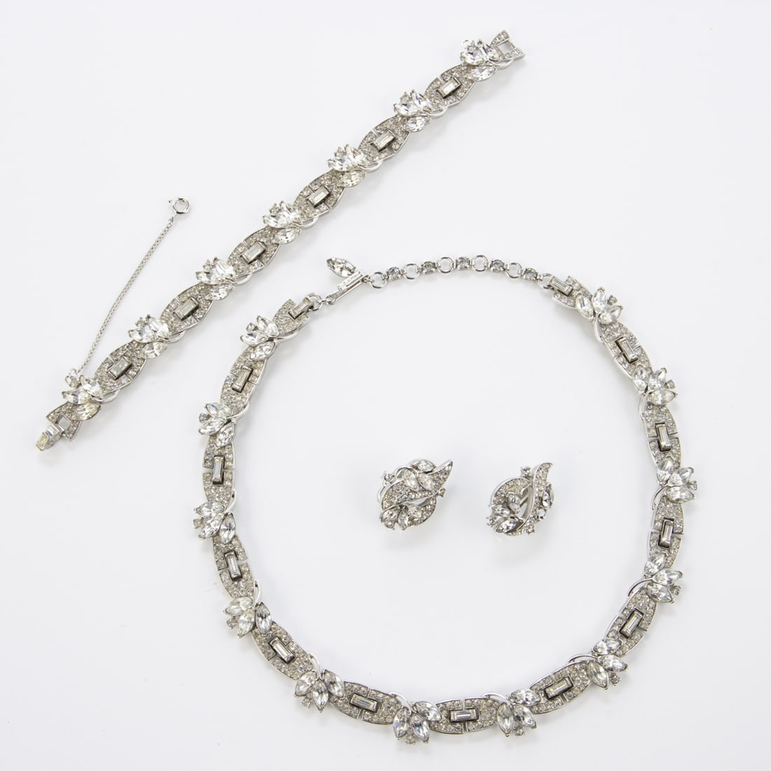 TRIFARI Alfred Philippe - Vintage Strass Schmuckset (3 Teile): TRIFARI Alfred Philippe - Vintage Strass Schmuckset (3 Teile)New York, um 1950 - 1970. Collier, Armband und Paar Ohrclips. Metall, silberfarben mit Kristall-Strasssteine. Collier-D.: 12 - 13 cm, B. ca