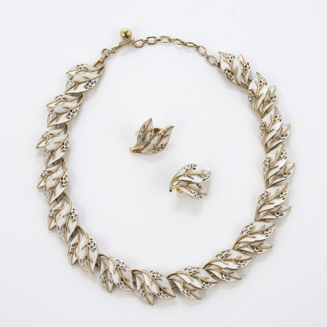 TRIFARI Alfred Philippe - Vintage weisses Emaille-Schmuckset (2 Teile): TRIFARI Alfred Philippe - Vintage weisses Emaille-Schmuckset (2 Teile)New York, um 1950 - 1970. Collier und Paar Ohrclips. Metall, goldfarben, Emaille. Collier-L. 39 cm, B. ca. 2 cm. Ohrclips 2 x 3 cm