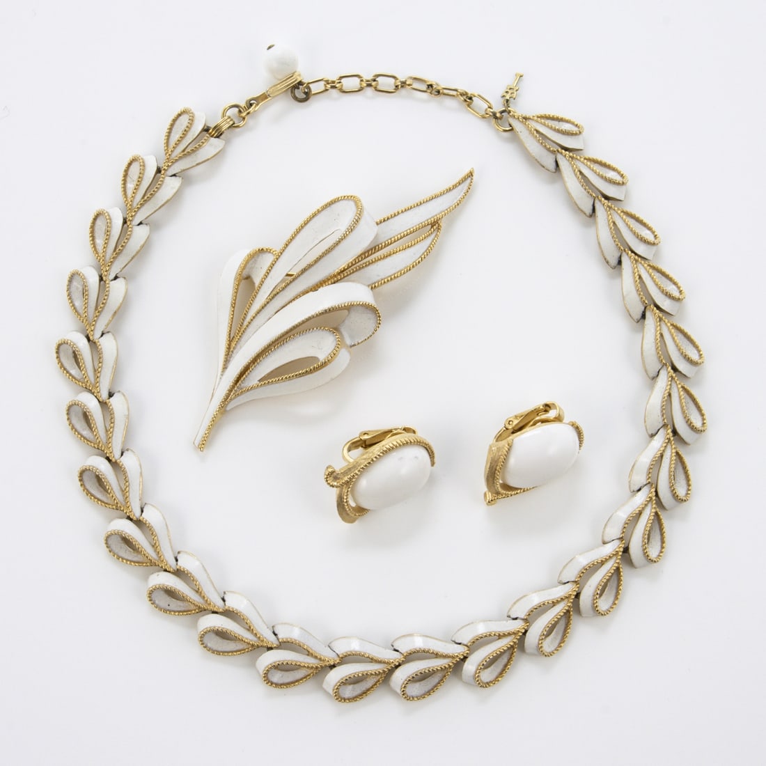 TRIFARI Alfred Philippe - Vintage weisses Emaille-Schmuckset (3 Teile): TRIFARI Alfred Philippe - Vintage weisses Emaille-Schmuckset (3 Teile)New York, um 1950 - 1970. Collier, Brosche und Paar Ohrclips. Metall, silberfarben, Emaille. Collier-L. 35 - 39 cm, B. ca. 1,5 cm.