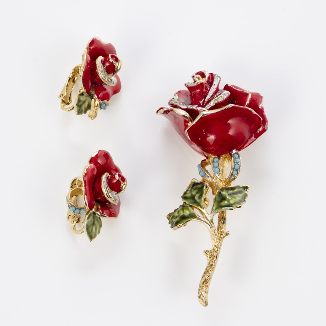 CORO - Vintage Rose Brosche und Paar Ohrclips: CORO - Vintage Rose Brosche und Paar OhrclipsCoro Cohn & Rosenberger Jewelry, New York, USA. Ca. 1950er Jahre. Brosche und Paar Ohrclips. Metall, goldfarben, Strasssteine, Emaille, blaue Glas-Cabochon