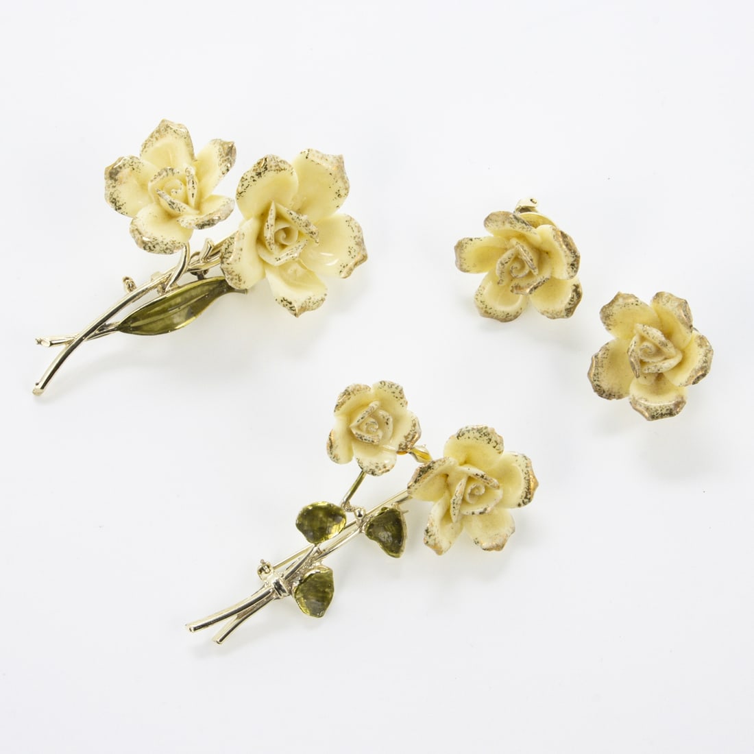 CORO - Vintage Schmuckset - Cremefarbene Porzellanrosen mit Emaille-Blaettern (3 Teile): CORO - Vintage Schmuckset - Cremefarbene Porzellanrosen mit Emaille-Blaettern (3 Teile)Cohn & Rosenberger Jewelry, New York, USA. Ca. 1950er Jahre. 2 Broschen und Paar Ohrclips. Metall, goldfarben. Cr
