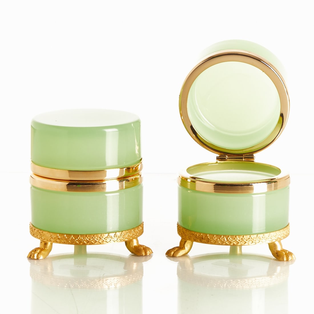 Pair of round lidded boxes on mounting with lion's feet - Art Deco.: Pair of round lidded boxes on mounting with lion's feet - Art Deco France, circa 1935-1940. Thick-walled, green opal glass, cut and polished. Brass mounting with hinge. Embossed mounting with lion's f