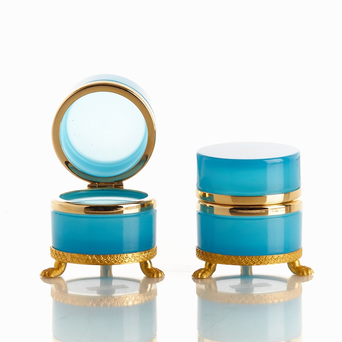 Pair of round lidded boxes on mounting with lion feet - Art Deco. France, circa 1935-1940.: Pair of round lidded boxes on mounting with lion feet - Art Deco France, circa 1935-1940. Thick-walled, blue opal glass, slightly translucent, cut and polished. Brass mounting with hinge. Embossed mou