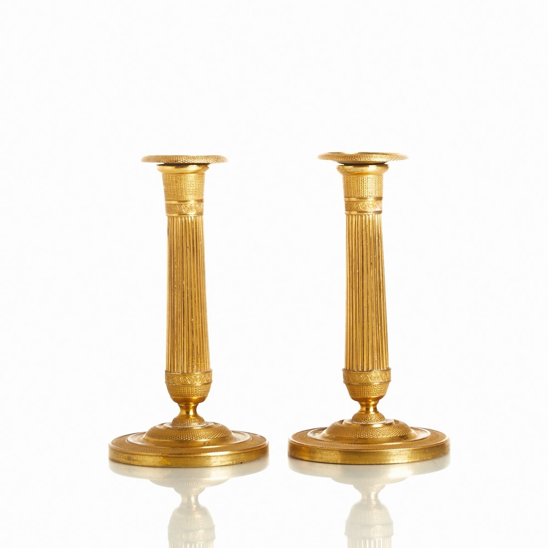 Pair of Empire Candlesticks: Pair of Empire candlesticks Probably France, 19th century. Brass, H. 17.5 cm, D. 9.5 cm. High-domed round base, finely chased frieze bands with ornamental decor, columnar nozzle with removable drip ca