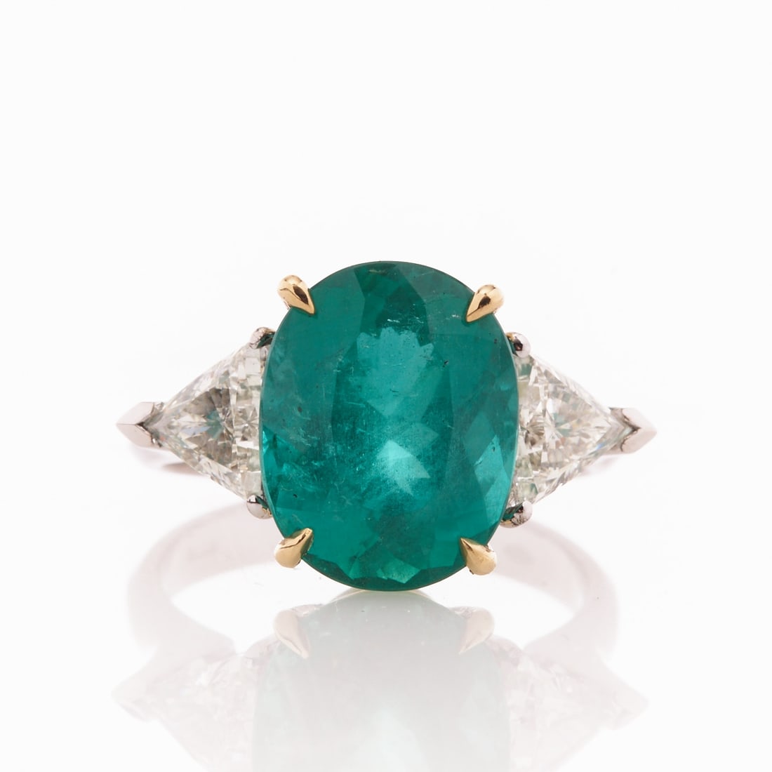 Ring with Brazilian emerald: Ring with Brazilian emerald. 750/- white gold and yellow gold, stamped. Total weight: 6.1 g. 1 emerald in oval cut of 5.75 ct. 2 triangle-cut diamonds totaling approx. 1.16 ct. Ring size 55. A current