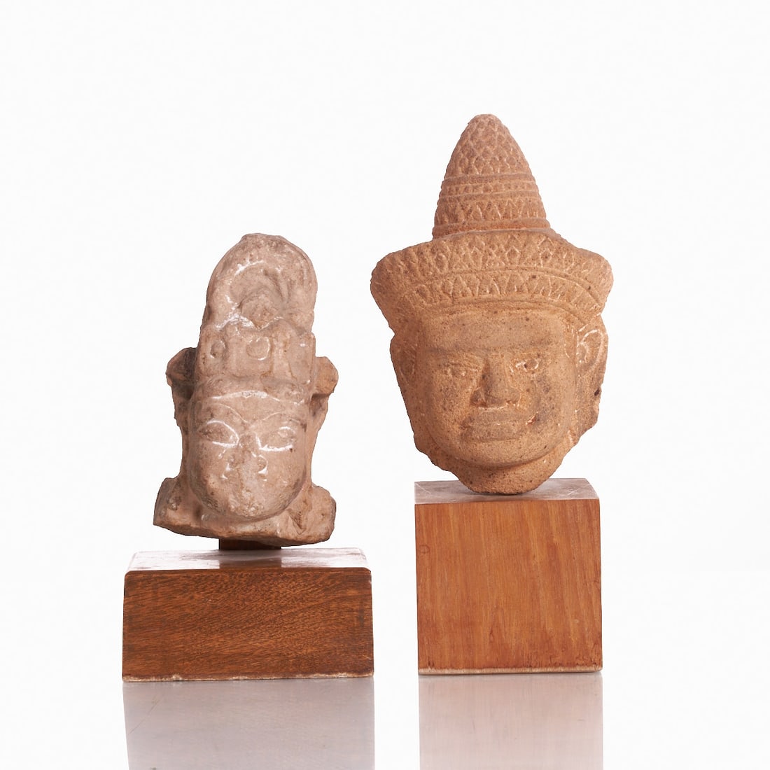 Two Sandstone Heads of Vishnu and Khmer: Two Sandstone Heads of Vishnu and Khmer India, probably 18th/19th century or earlier. Sandstone, mounted on wooden bases. Dimensions without base: approx. 20.5 x 13.5 x 11 cm and 17 x 9.5 x 7.5 cm.