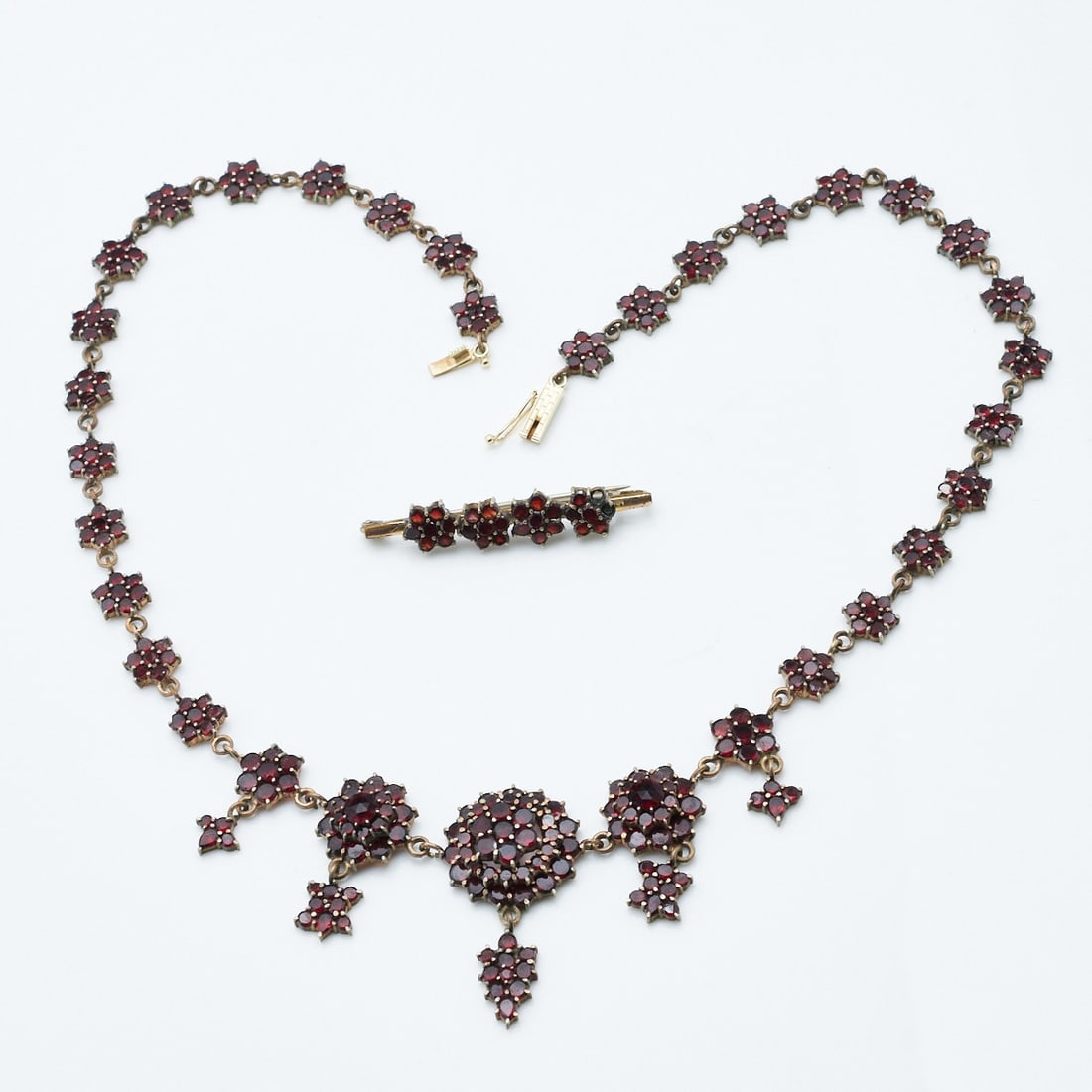 Garnet Necklace and Brooch: Garnet necklace and brooch Tombac. Weight: 27.9 g. Various garnets. L. 46 cm. W. 4 cm. Brooch L. 4.2 cm. W. 0.7 cm. Box clasp. Signs of wear.