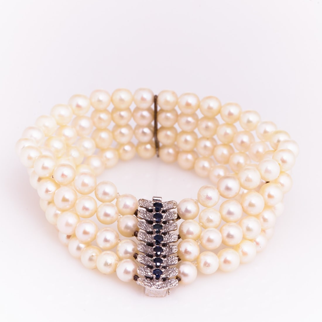 Four-Row Pearl Bracelet with Sapphire Clasp: Four-Row Pearl Bracelet with Sapphire Clasp 585/- white gold, stamped. Weight: 46.4 g. Hallmark: JKa. Various cultured pearls. 7 round cut sapphires, total approx. 0.35 ct. L. 19.2 cm. W. 2.8 cm. Box 