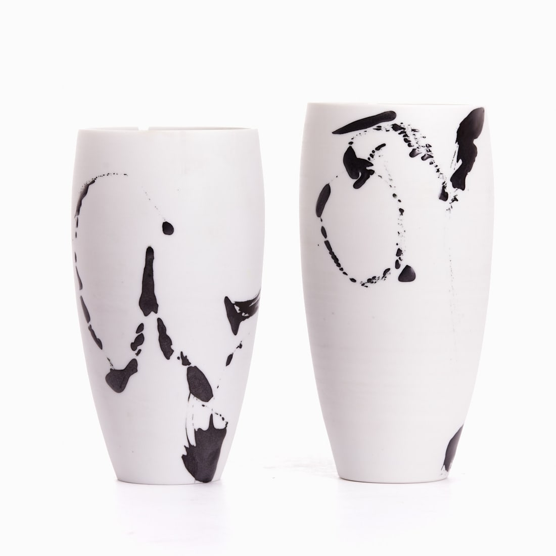 2 different mugs. Karin Bablok, Hamburg.: 2 different mugs Karin Bablok, Hamburg. Porcelain, white, glazed inside. Painted on the outside: gray-metallic, irregularly spot-distributed elements. Each marked under the base. H. 12.5 cm and H. 13
