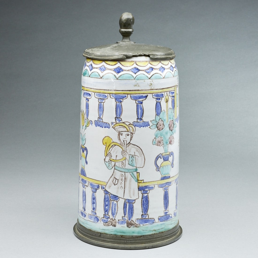 Cylindrical jug - Musician in front of a railing in a landscape. 19th century.: Cylindrical jug - Musician in front of a railing in a landscape 19th century. Faience, reddish shard. Whitish engobe. Painted in colorful sharp-fire glazes. Pewter base ring and pewter thumb rest