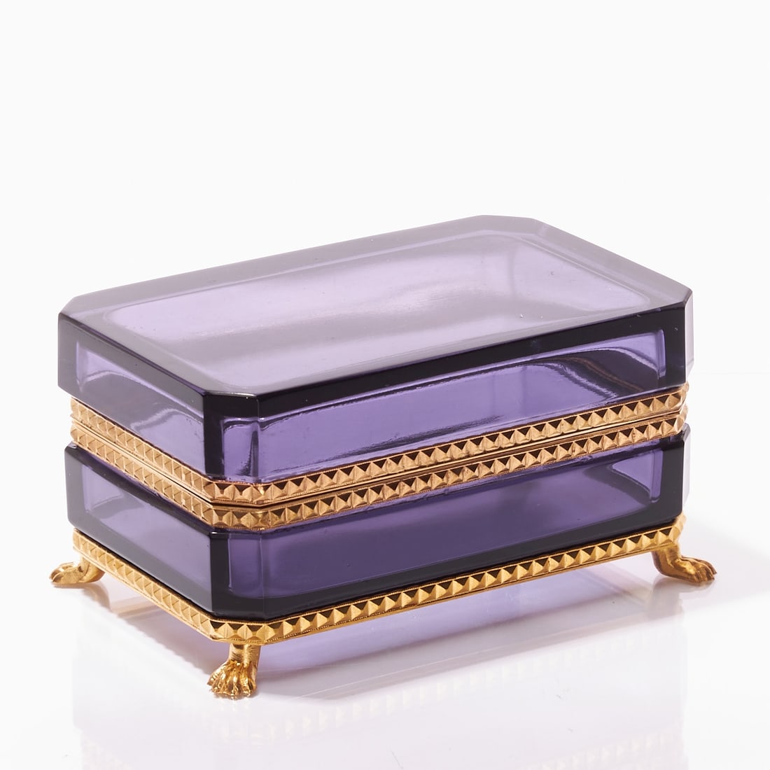 Octagonal lidded box on mount with lion feet - Art Deco. France, circa 1935-1940.: Octagonal lidded box on mount with lion feet - Art Deco France, circa 1935-1940. Thick-walled, violet glass, cut and polished. Edges cut. Gilt brass mount with hinge. Decorated brass mount with
