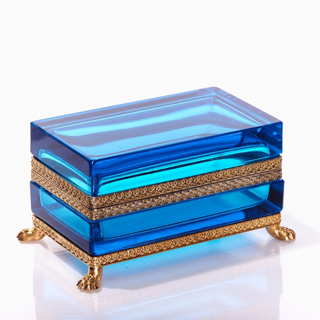 Rectangular lidded box on mounting with lion feet - Art D?©co. France, circa 1935-1940.: Rectangular lidded box on mounting with lion feet - Art Déco France, circa 1935-1940. Thick-walled, blue glass, cut and polished. Gilt brass mounting with hinge. Embossed mounting with relief a