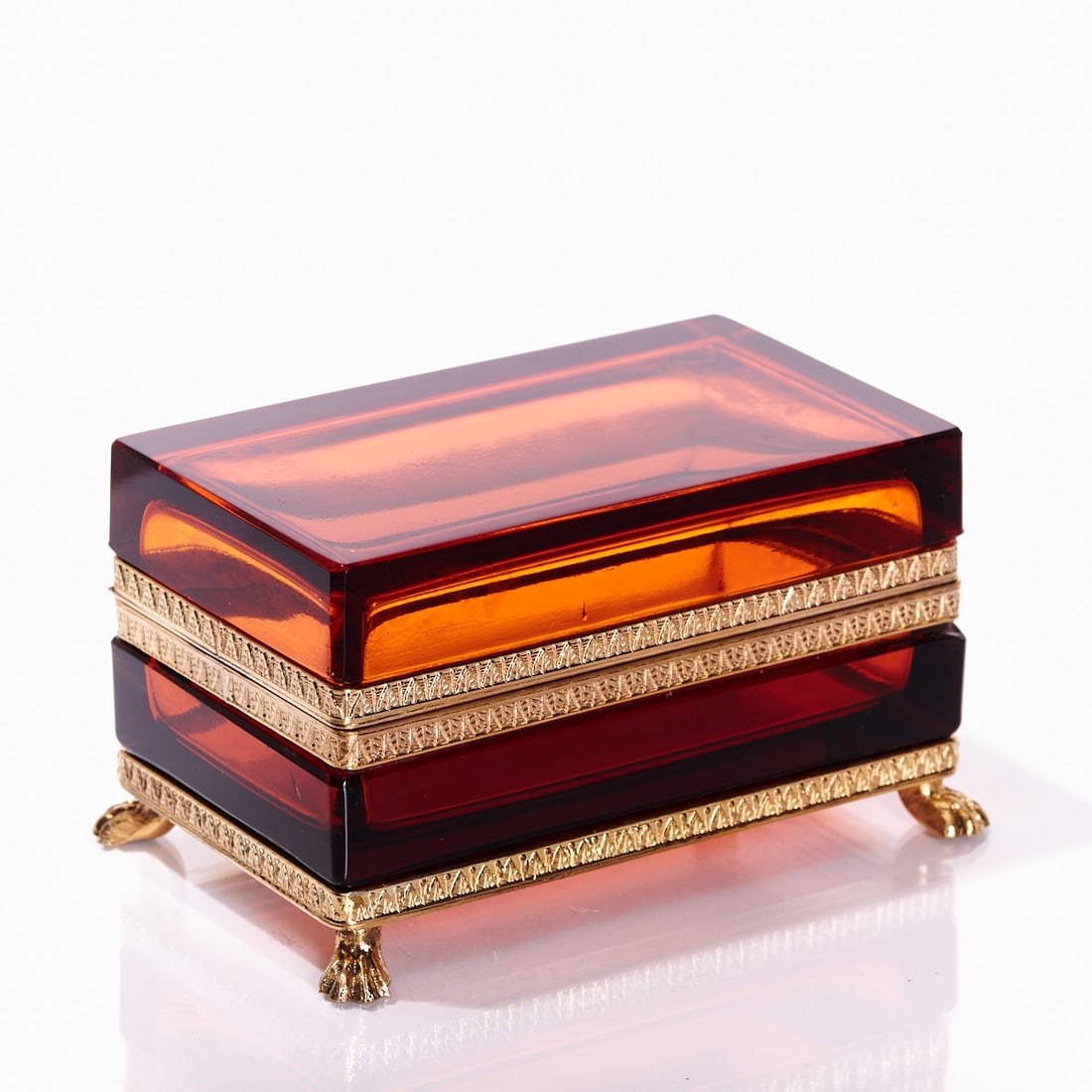 Rectangular lidded box on mounting with lion's feet - Art D?©co. France, circa 1935-1940.: Rectangular lidded box on mounting with lion's feet - Art Déco France, circa 1935-1940. Thick-walled, amber-colored glass, cut and polished. Gilded brass mounting with hinge. Relief mounting wi
