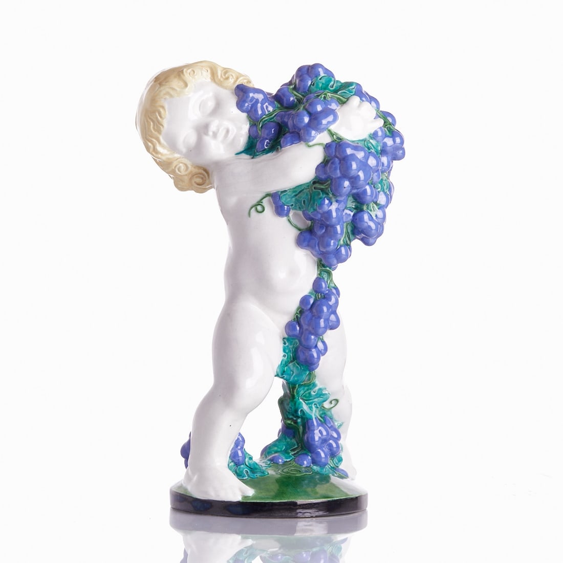 Michael Powolny. Putto with Grapes (Autumn) - Execution: Wiener Keramik, c. 1907.: Putto with Grapes (Autumn) - Michael Powolny Michael Powolny - Execution: Wiener Keramik, c. 1907. Earthenware, white body, polychrome glazed. On the base, two embossed marks: Wiener Keramik and artis