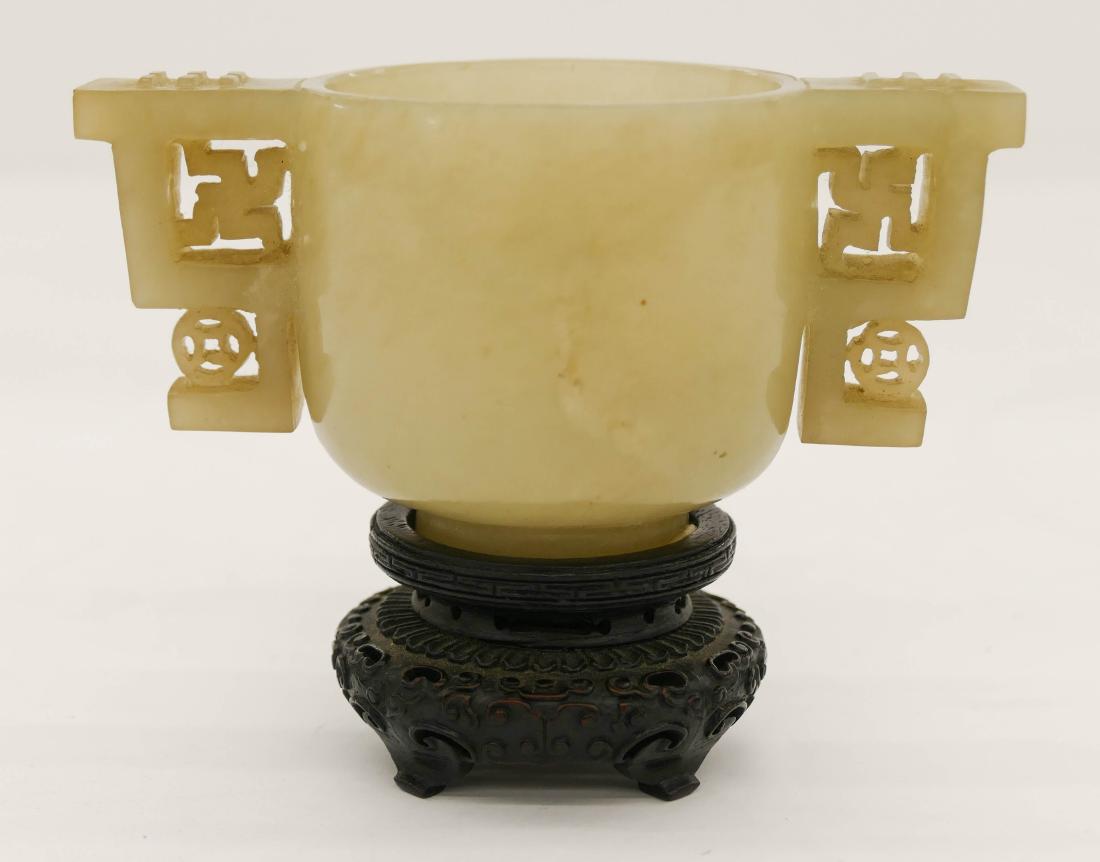 Fine Chinese Jade Libation Cup on Stand 3''x4.25''. An: Fine Chinese Jade Libation Cup on Stand 3''x4.25''. An intricately carved pale celadon jade pierced handle cup with relief buddhist trigrams on handles. Fine carved rosewood fitted base. Excellent con