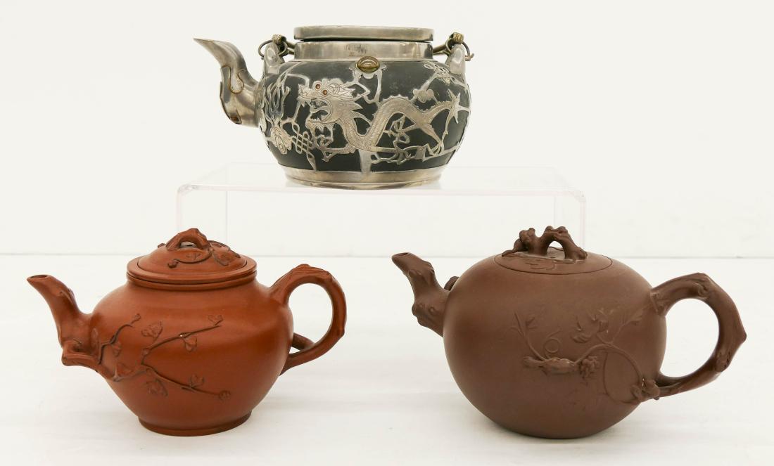 3pc Chinese Yixing Clay Teapots. Includes a black: 3pc Chinese Yixing Clay Teapots. Includes a black paktong mounted dragon teapot 4''x7.5'', a dark crabstock handled teapot (cracked near handle) 4''x8'', and a red yixing crabstock teapot with liner 4