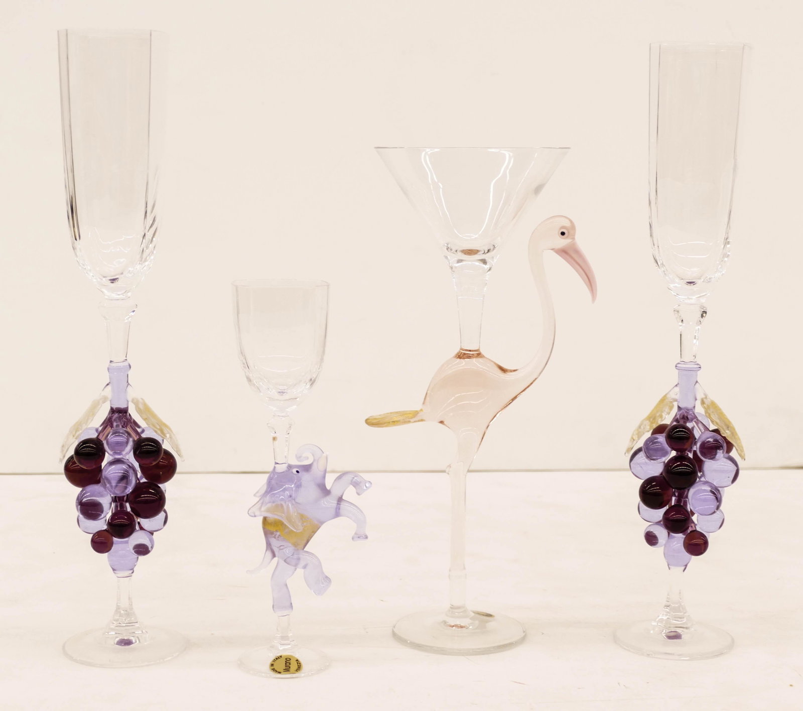 4pc Murano Glass Figural Stem Goblets 7.5'' to 12'': 4pc Murano Glass Figural Stem Goblets 7.5'' to 12'' Tall. Includes a pair of grape stems, a flamingo martini glass, and a elephant stem. Two smaller have original labels. Excellent condition.