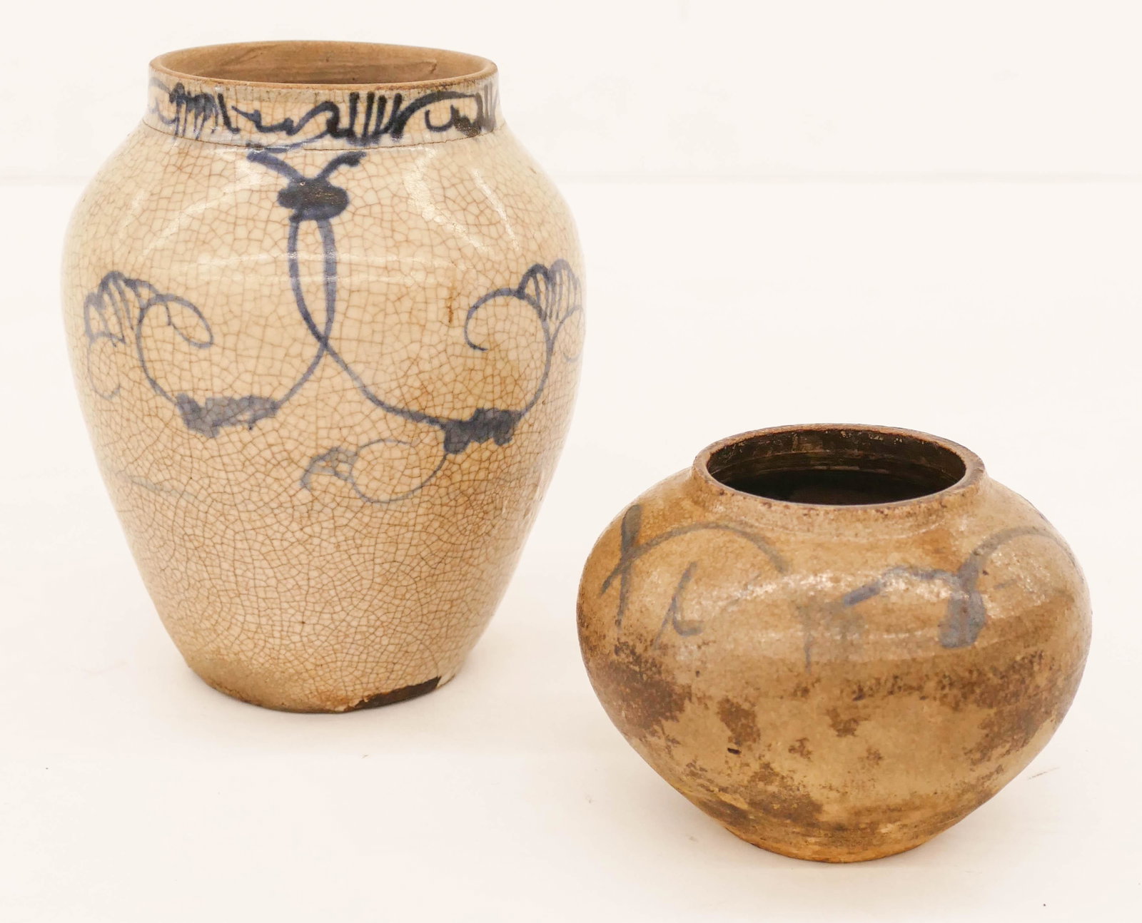 2pc Korean Joseon Blue and White Decorated Jars 3'': 2pc Korean Joseon Blue and White Decorated Jars 3'' to 5.75'' Tall. A duo of blue underglaze decorated ceramic jars with scrolling motifs. Larger jar has burn and glaze flake to bottom edge. Smaller j
