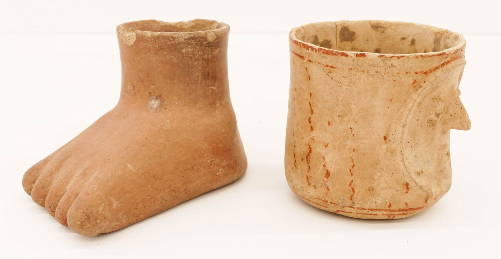2pc Colima Pre Columbian Portrait Cylinder and Foot: 2pc Colima Pre Columbian Portrait Cylinder and Foot Vessel. Includes a bicolor face vessel 5''x5'' (cracked with edge chipping) and a figural redware foot vessel 4.75''x7'' (some edge chipping). 200 B