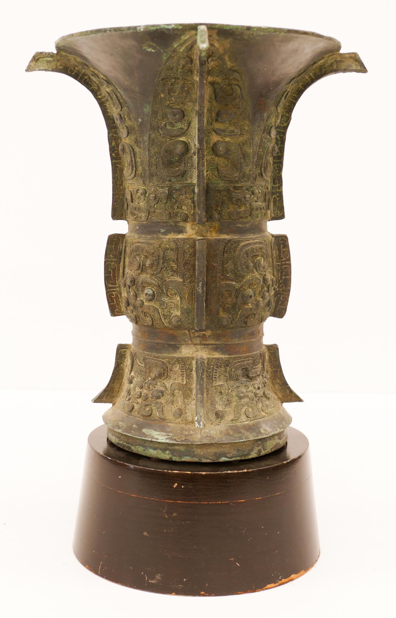 Chinese Ming Archaic Bronze Zun Vessel: Chinese Ming Archaic Bronze Zun Vessel 12.5''x11''. Archaistic decorated bronze wine vessel with taotie mask motifs. Comes on ebonized wood pedestal 3.5''x7.5''. Scattered verdigris patina from age wi