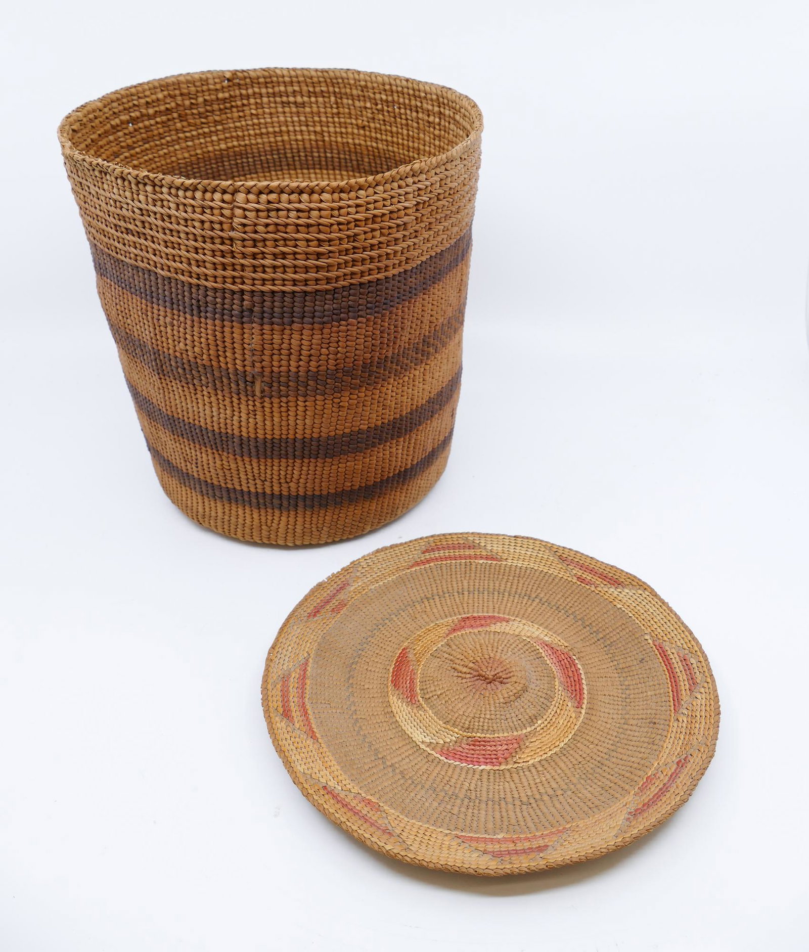 2pc Old Haida & Tlingit Indian Baskets: 2pc Old Haida & Tlingit Indian Baskets. Early 20th century. Includes Haida banded cylinder bark basket (8x7.5'' with old 4'' split repair), and Tlingit geometric band basketry tray (7.5'' diameter in 