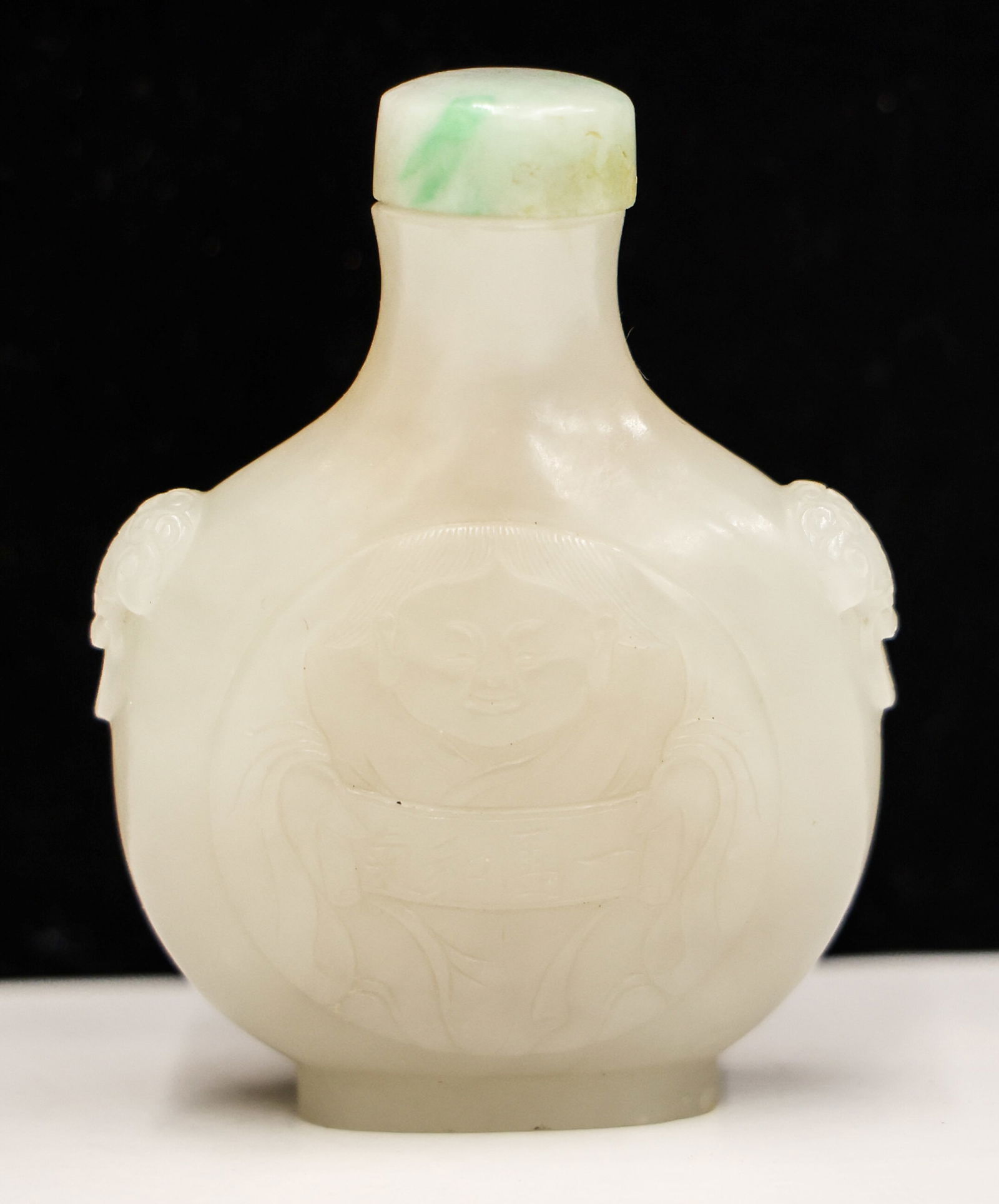 Chinese White Jade Boy with Scroll Snuff Bottle: Chinese White Jade Boy with Scroll Snuff Bottle 2.5''x2''. Mutton fat white coloring. Intricate relief carving of boy with scroll and mask with ring handles. Jadeite stopper and well hollowed form. Ex