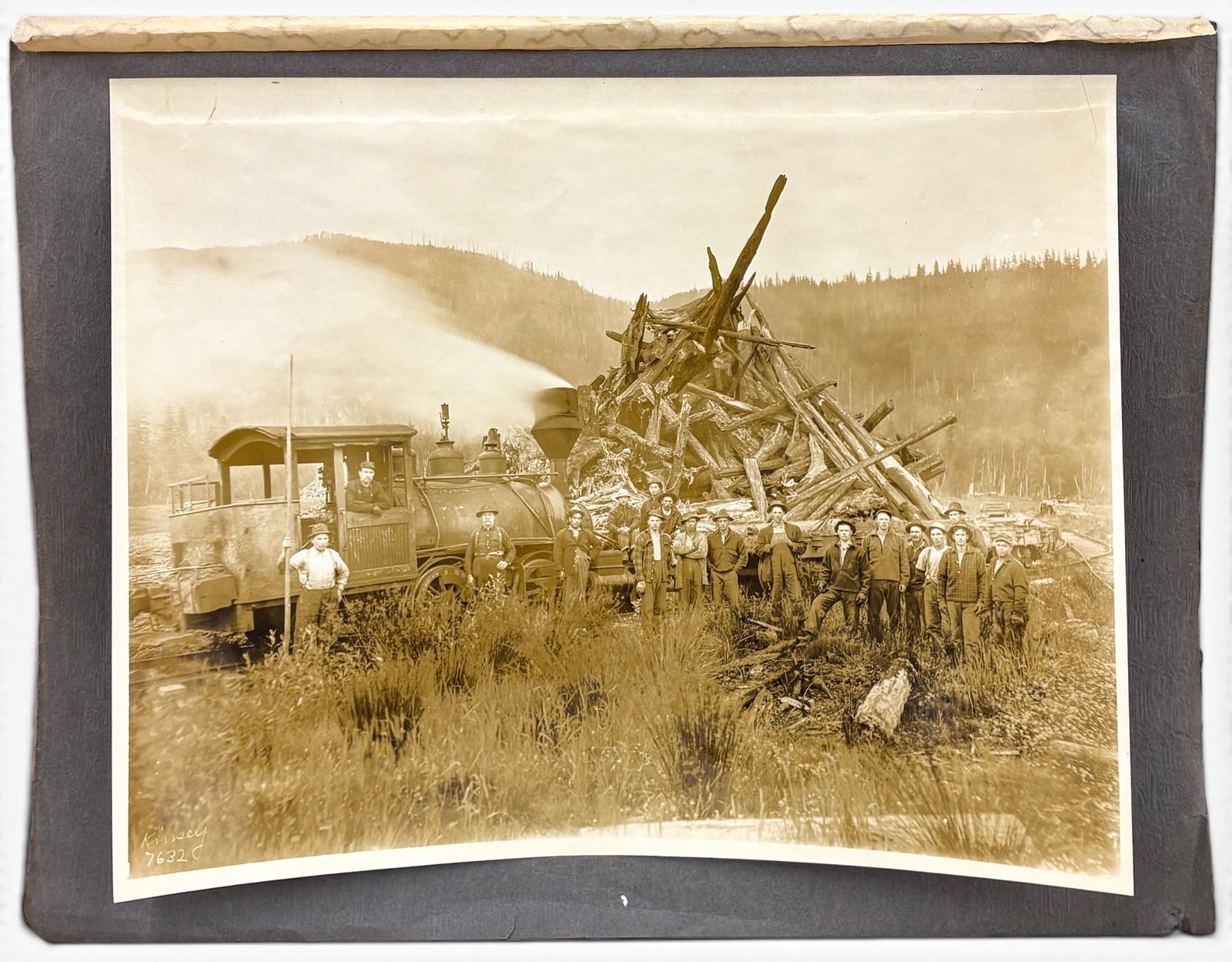 Kinsey Bros. "Train & Wood Pile" Photograph: Kinsey Bros. "Train & Wood Pile" Photograph 11"x14" Sheet 12.75"x16.5" Mounted. Signed lower left and numbered 7632. Hinged at top, minor creasing, minor stains at top.