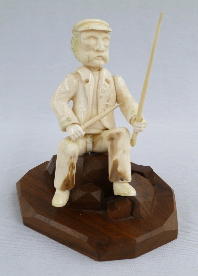 Alaskan Carved Ivory Seated Fisherman or Net Mender: Alaskan Carved Ivory Seated Fisherman or Net Mender 7.5''x3.5''. Nautical captain is made of solid ivory and sits on carved wood base. He holds replaced sewing tools in hands. Old glue repair to waist