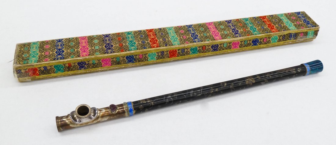 Chinese Enameled & Silver Inlaid Opium Pipe in Silk: Chinese Enameled & Silver Inlaid Opium Pipe in Silk Box. It measures 15.5'' long x 1'' wide. Depicting figures, birds, and blossoming flowers amongst a landscape. 19th/20th century.