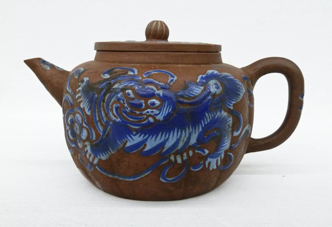Chinese Zisha Enamel Foo Lion Yixing Teapot: Chinese Zisha Enamel Foo Lion Yixing Teapot 3.25''x6.25''. Depicts a foo dog and blossoming flowers in blue enamel. Unmarked with red chinese export stamp on bottom. Slight chip to spout. Qing dynasty