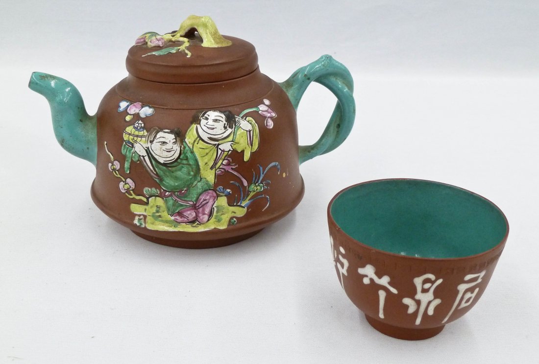 Antique Chinese Zisha Enameled Yixing Teapot & Cup.: Antique Chinese Zisha Enameled Yixing Teapot & Cup. Teapot has two enameled figures and measures 4.75''x7''. Impressed character mark under lid and base. Chips to bottom edge of lid. 2'' cup has been 