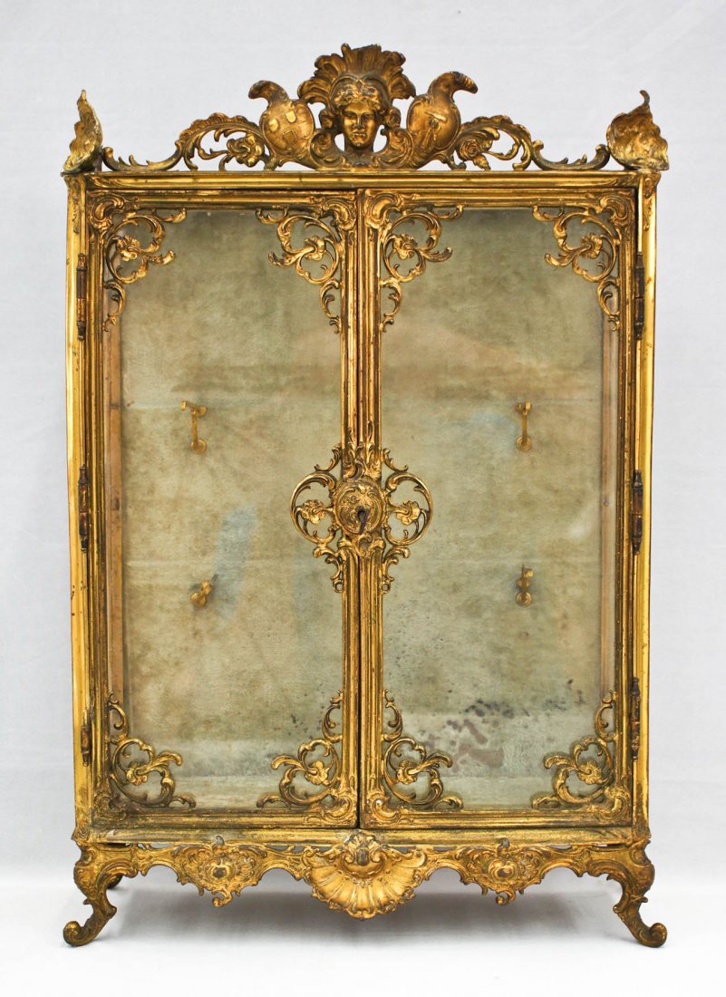 French Dore Bronze Rococo Miniature Curio Cabinet: French Dore Bronze Rococo Miniature Curio Cabinet 21.25''x14.5''x6.25''. Gilt bronze body with glass shelves. Small chip to figural head finial. Complete with fitted glass shelves. 19th century.