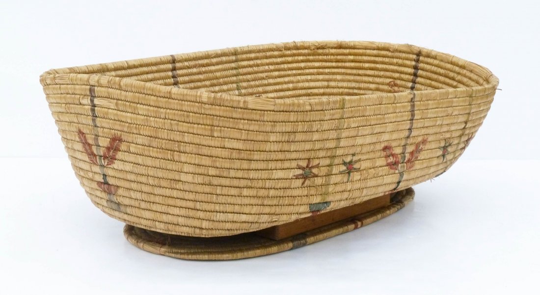 Large Yupik Coiled Indian Basket Cradle: Large Yupik Coiled Indian Basket Cradle 7.5''x25''x18''. Alaskan native basket with stylized floral motifs. Overall edge wear with wood blocks supporting the bottom of the basket. Early to mid 20th ce