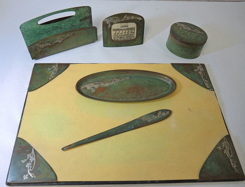 Arts & Crafts Six Piece Silver On Copper Desk Ensemble: Consists of blotter with corners, oval tray, letter opener, calendar, oval inkwell, letter caddy. Blotter measures 12" x 18"