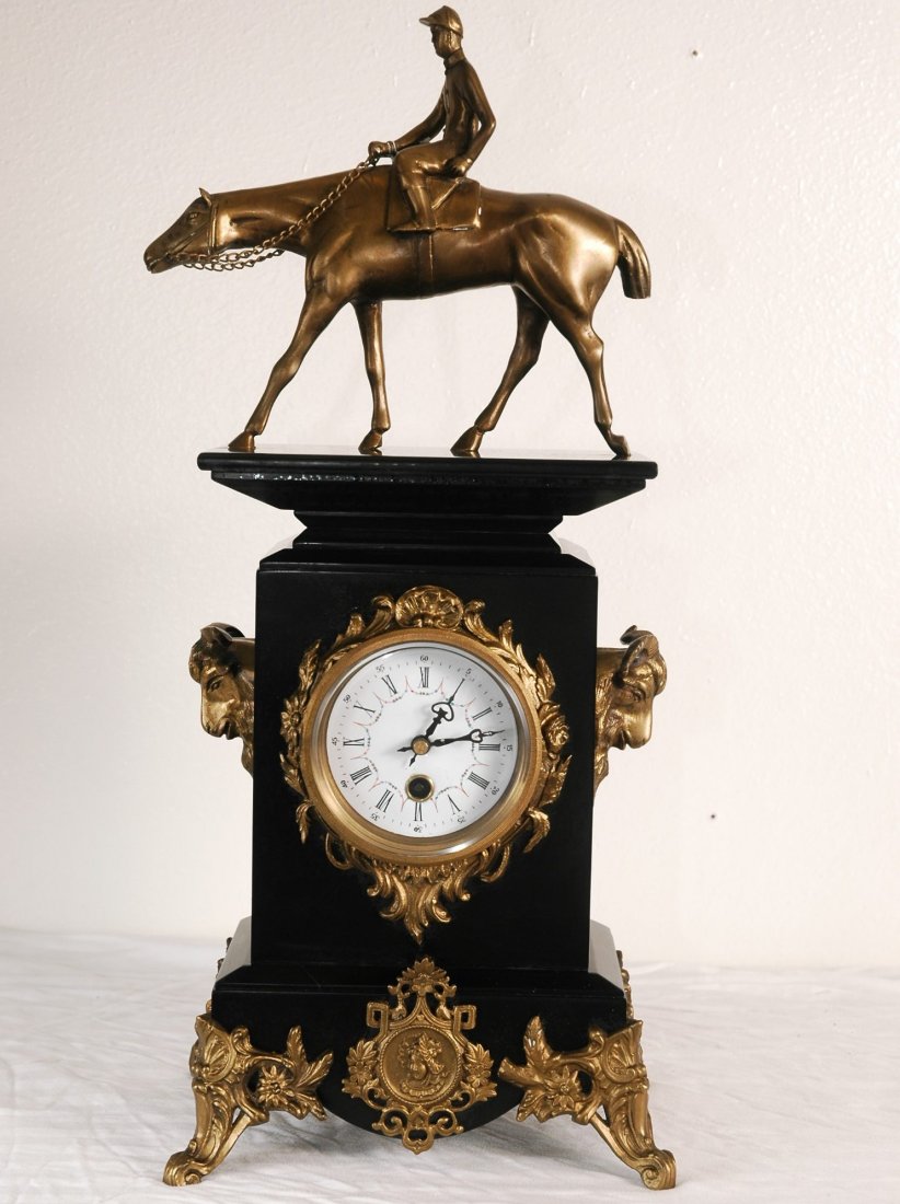 Marble and Bronze Clock: Black marble and bronze mantle clock with bronze man riding horse on top. Bronze rams protrude from the side, rests on four marble feet. 19"H x 8"W.